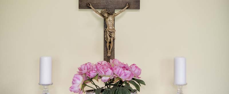 Dieses Bild zeigt ein Kreuz, zwei Kerzen und Blumen